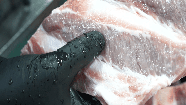 Person inspecting raw meat with gloved hands