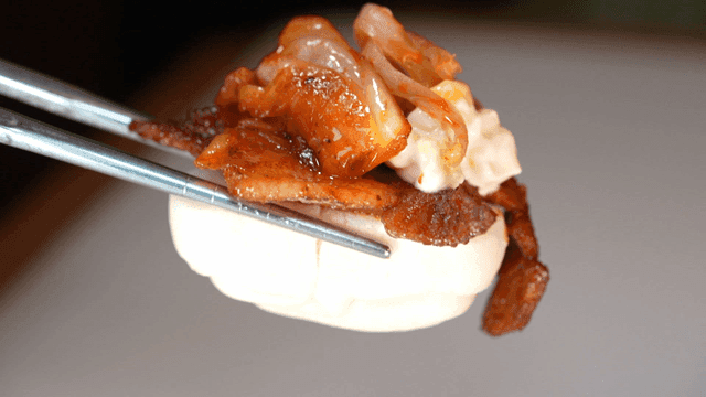Chopsticks picking up stir-fried pork on steamed bun