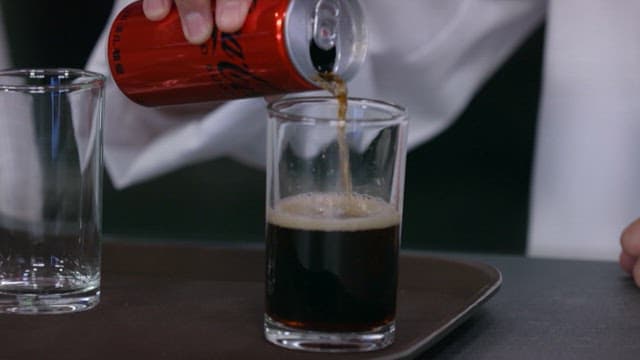 Pouring cola from a red can into a clear glass.