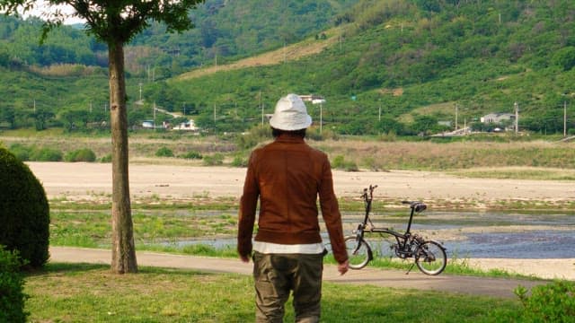 녹색 강변 길에 자전거를 세운 남자