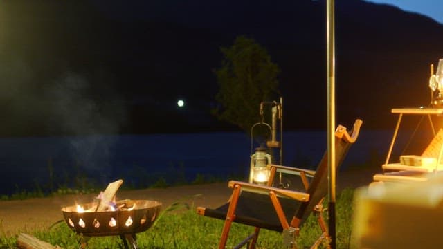 Evening camping by the serene riverside with a person sitting beside a campfire