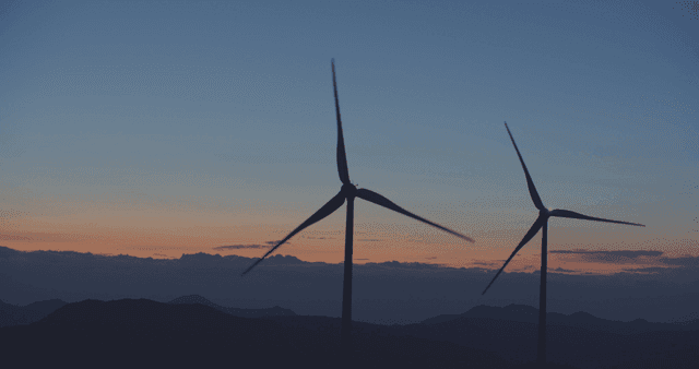 산 너머 일몰의 빠르게 돌아가는 풍력 터빈
