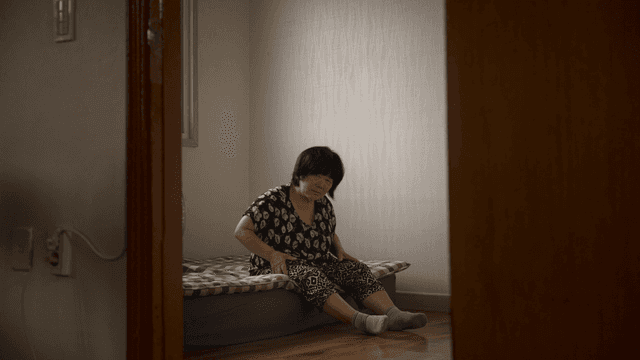 Elderly woman massaging her leg while sitting on a bed