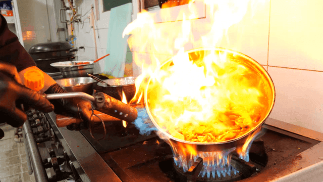 Chef burning flames on frying pan with torch