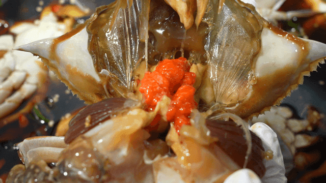 Hands cutting through soy sauce marinated crab with roe