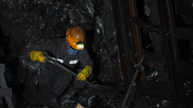 Miner working in a dark underground tunnel with a shovel