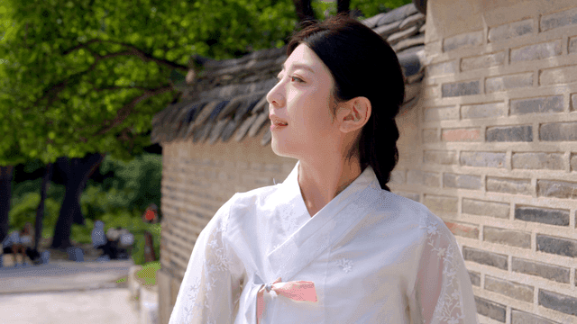 Woman in hanbok standing by a traditional wall