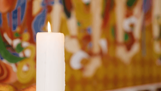 Candle burning in front of a colorful mural