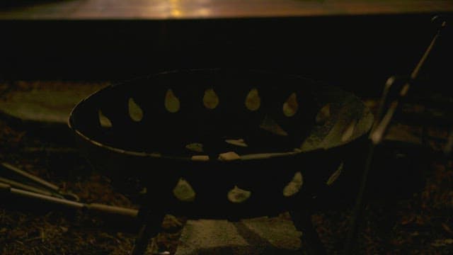 Campfire is lit in a brazier at night using a torch and firewood