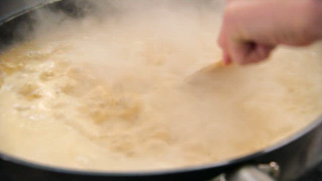 Stirring boiling sauce in a pot with a wooden spatula