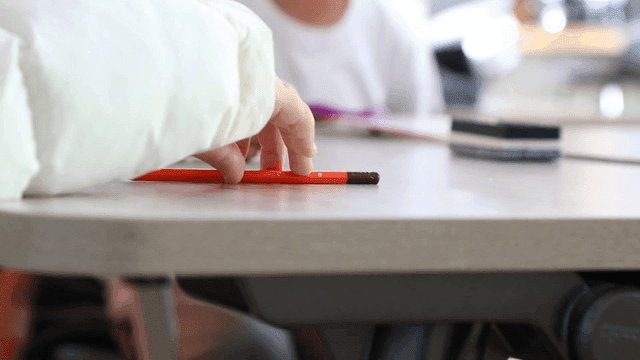 Child holding red pencil in classroom