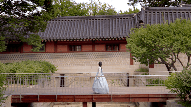 Woman in hanbok walking by a traditional Korean building