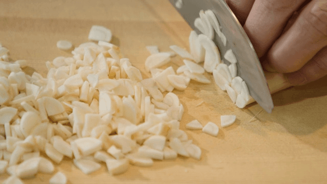 나무 도마 위에서 마늘을 써는 모습