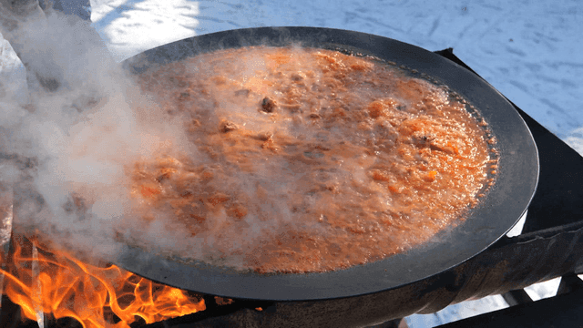 Chicken stew cooked on large pot lid over fire