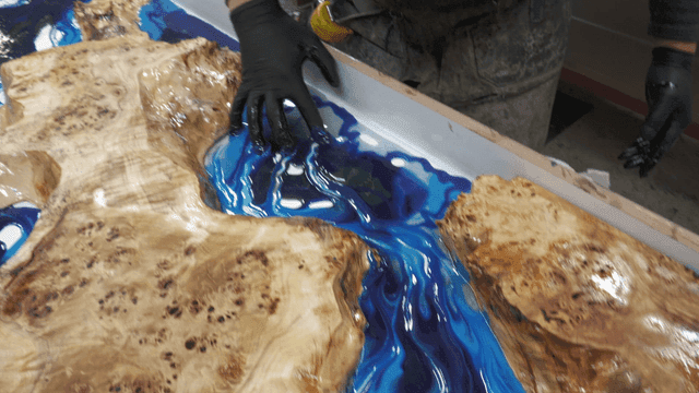 Hands applying blue epoxy resin to wood