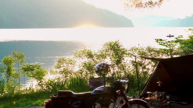 Campsite by a serene lake at sunrise with motorbike and tent