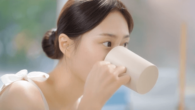 욕실 거울 앞에서 양치컵에 물을 받아 입을 헹구는 여성