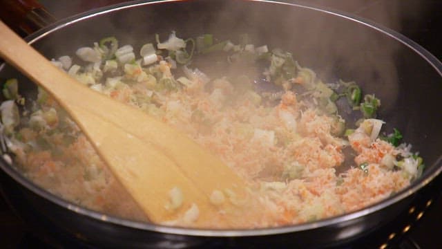 Stir frying vegetables and crab meat with a wooden spatula in a pan