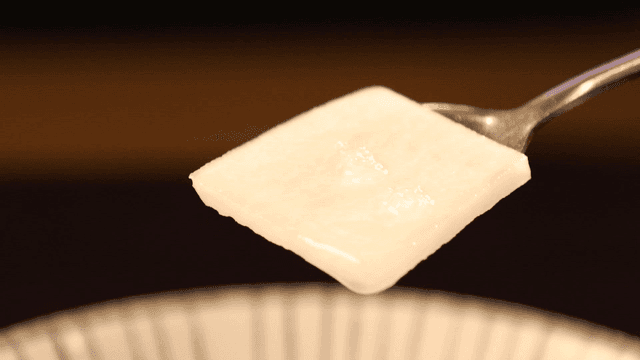 Spoon scooping out dongchimi radish from clear broth