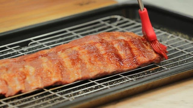 Brushing sauce on ribs on a grill