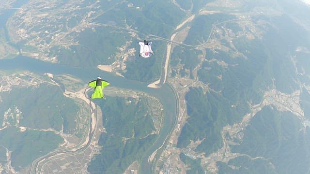 지면을 배경으로 날아오르는 윙슈트 모험가들