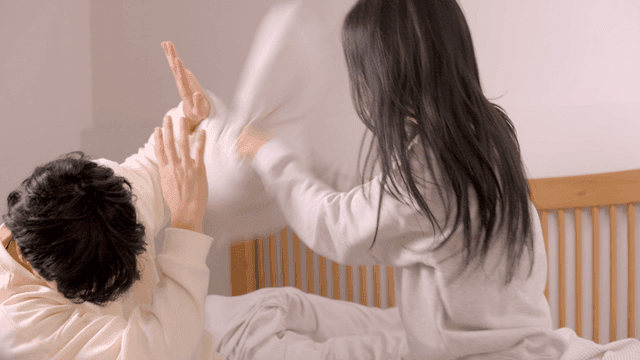 Playful couple pillow fight in cozy bedroom