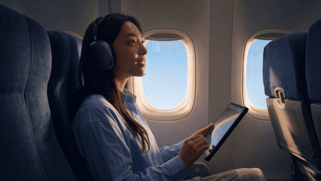 Woman wearing wireless headset and looking at tablet on airplane