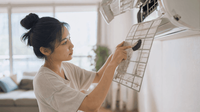Woman cleaning dust from air conditioner filter with brush
