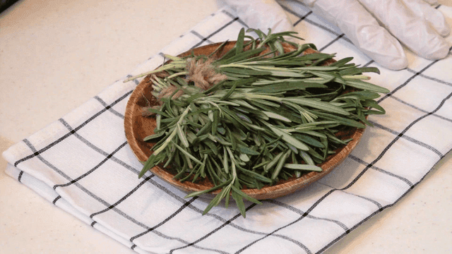 Fresh rosemary in wooden bowl on cloth in kitchen
