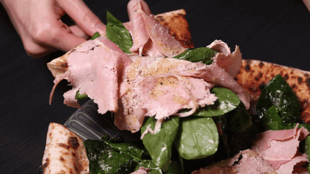 A hand picking up a slice of pizza with ham and spinach