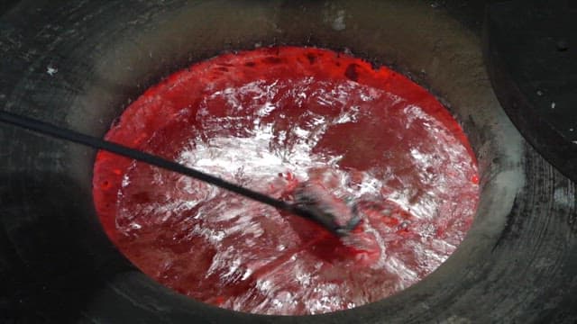 큰 산업용 용기에서 고온에 녹은 쇳물을 젓는 모습