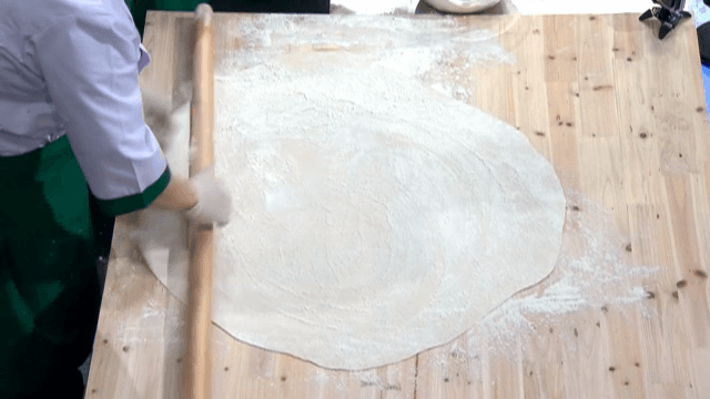 나무 테이블에서 반죽을 밀고 있는 요리사