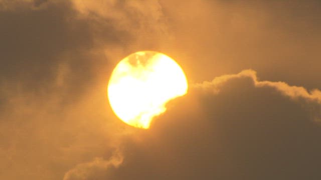 The sun partially obscured by clouds at dusk