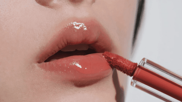 Woman applying red lipstick to shiny lips