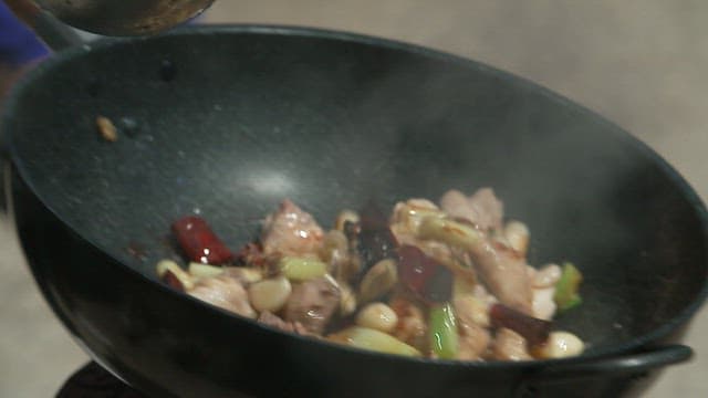 Sauce and meat being stir-fried over high heat in a large wok