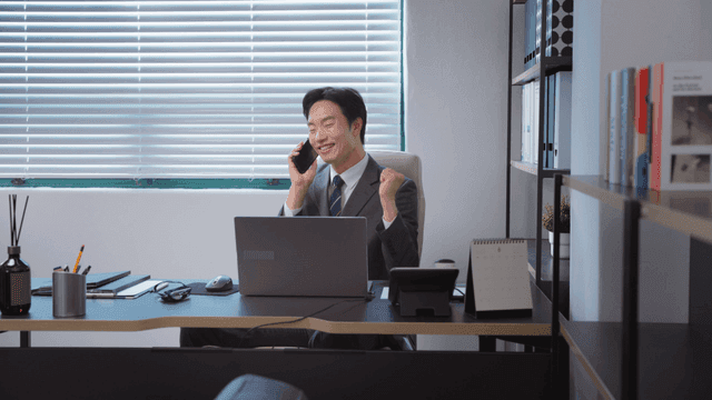 A man cheering while making a phone call in his office