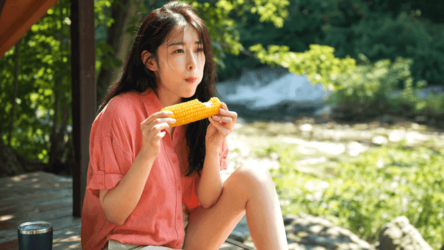 여름 강가에서 옥수수를 먹는 여성