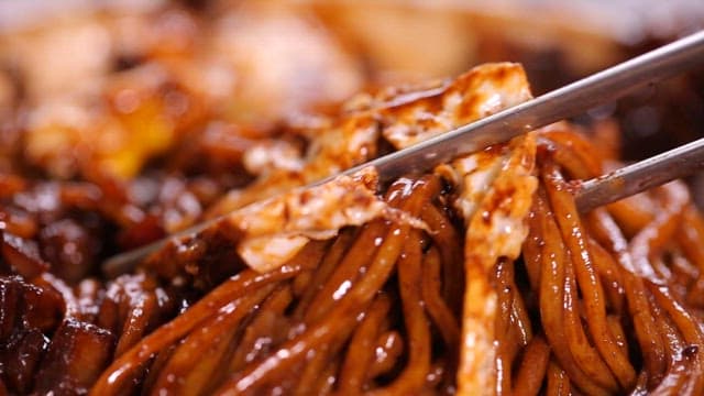 Chopsticks lifting noodles in thick black bean sauce