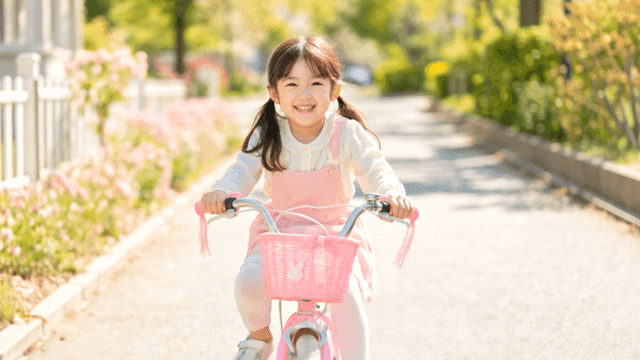 Young girl riding pink bicycle on sunny day