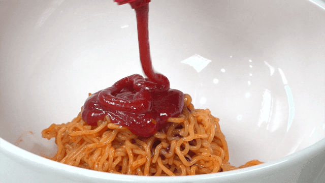 Spicy sauce poured over bibim noodles in a bowl