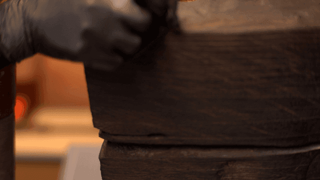 검은 장갑을 끼고 나무 조각품을 연마하는 장인