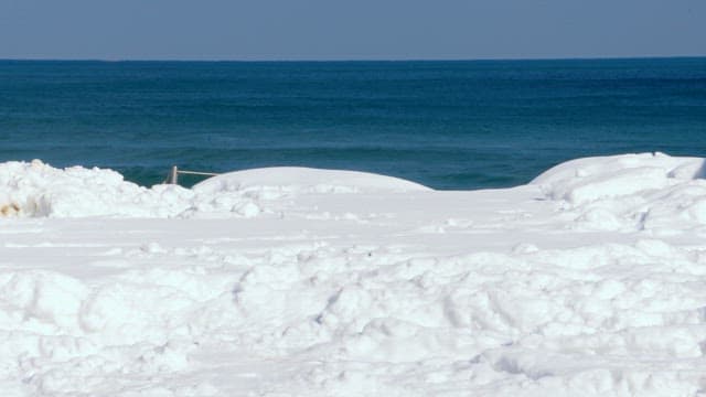 Person walking on a snowy beach by the sea