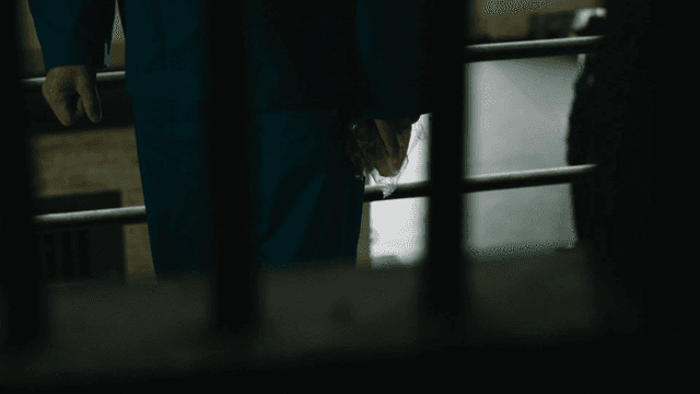 Prisoner holding piece of plastic-wrapped bread beyond bars.