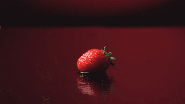 Red strawberries fallen into shallow water on a dark red background