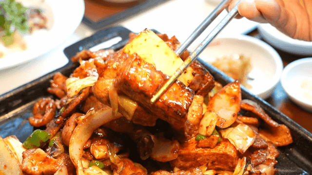 Chopsticks picking up stir-fried pork on hot iron plate