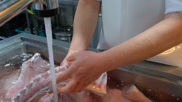 Washing large cuts of raw meat under running water in a kitchen