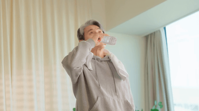 Elderly man drinking water indoors