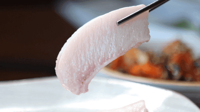 Fresh yellowtail belly sashimi picked up with chopsticks