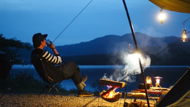 Man relaxing at a lakeside campsite with lights on