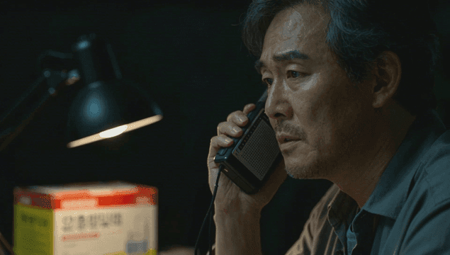 어두운 방에서 무전기로 대화하는 중년 남자